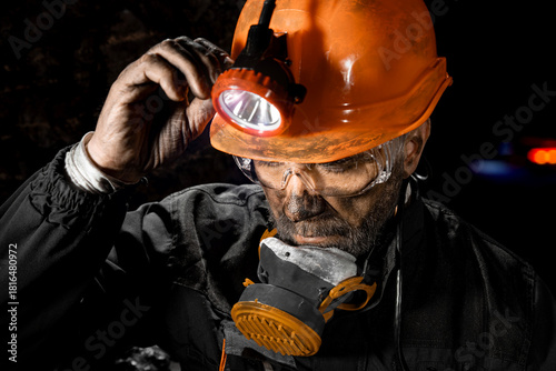 Tableau sur toile Coal miner with a dirty face in black dust, wearing a protective helmet with a flashlight, filtering respirator and work clothes for working in mine
