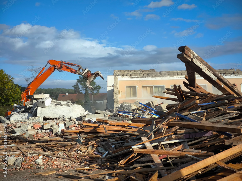 Fototapeta premium Escavadora a operar na demolição de um prédio, posicionada sobre uma vasta pilha de destroços, composta por pedaços de madeira danificadas, tijolos e fragmentos de concreto