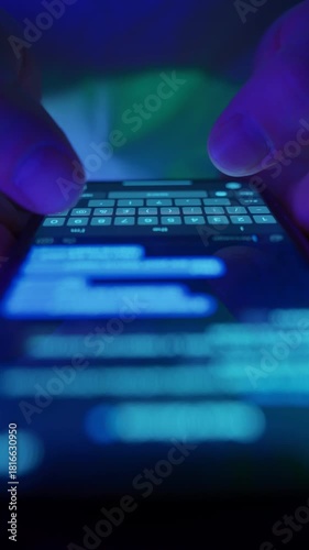 Close-up of fingers typing text message on smartphone keyboard in dark environment. Macro view of chatting on phone. Modern communication, messaging apps and social media. Vertical video