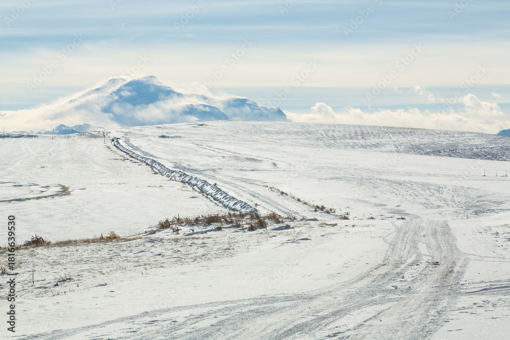 Naklejka premium View over the snow-covered peak of Elbrus in winter and the snowy road to it. Caucasus, Russia
