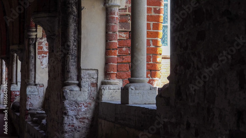 Architectural view of Riga Dome Cathedral’s red brick walls and aged stone columns from shaded corridors, revealing medieval textures and sacred atmosphere.