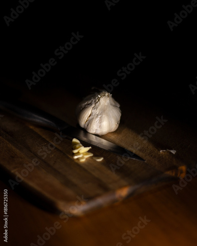 Close-up of a bulb of garlic on a wooden chopping board with a sliced clove of garlic