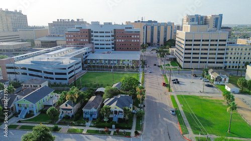 Grassy vacant land near multi-story research, administrative buildings form coastal academic hub, surrounded by green buffers, roadways, port infrastructure visible in distance, Galveston, Texas