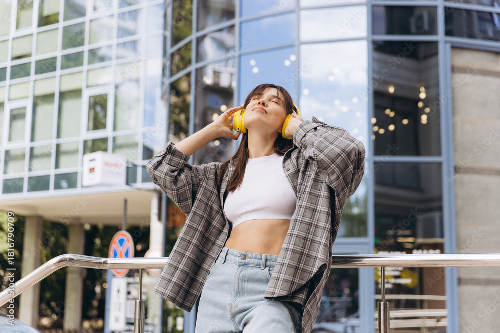 Fototapeta premium Young woman enjoying music with headphones in city