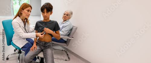Senior woman looking at physician perform chest auscultation on grandson using stethoscope during routine examination