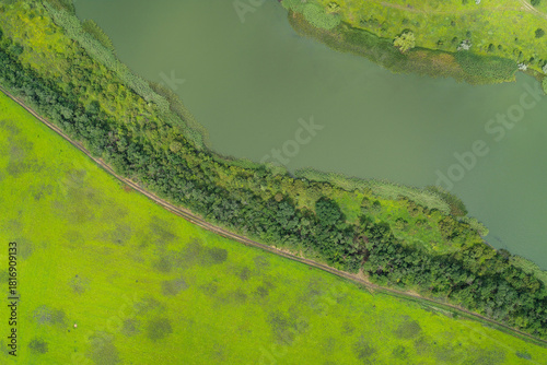Aerial view of clean water body bordering a green agricultural field, separated by natural bush and forest line. Conceptual background for water resources, ecology, conservation, and land management.