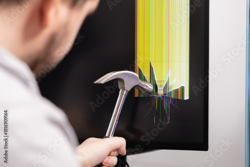 Angry individual smashes a computer monitor screen with a hammer, causing severe cracks and vibrant lines, symbolizing technology frustration