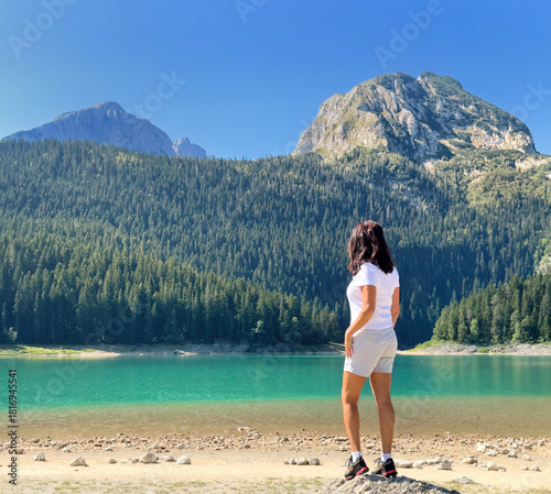 Woman looks over turquoise Crno Jezero (Black Lake) beneath Durmitor mountains, Montenegro. Ideal for: Balkan tourism, hiking blogs, vanlife journeys, outdoor lifestyle campaigns.  