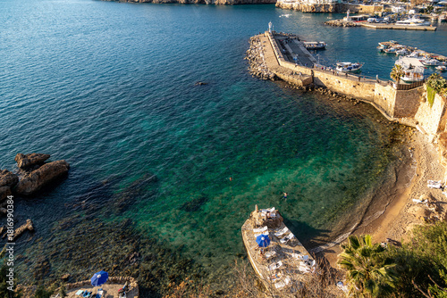 Fototapeta Naklejka Na Ścianę i Meble -  Aerial view of Mermerli Beach's turquoise waters and rocky shore near Kaleici marina. A few swimmers and sunbathers enjoy the sunny winter day in Antalya, Turkey, Mediterranean.

