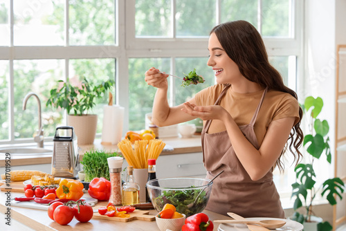 Canvas Print Young woman eating vegetable salad at table in kitchen