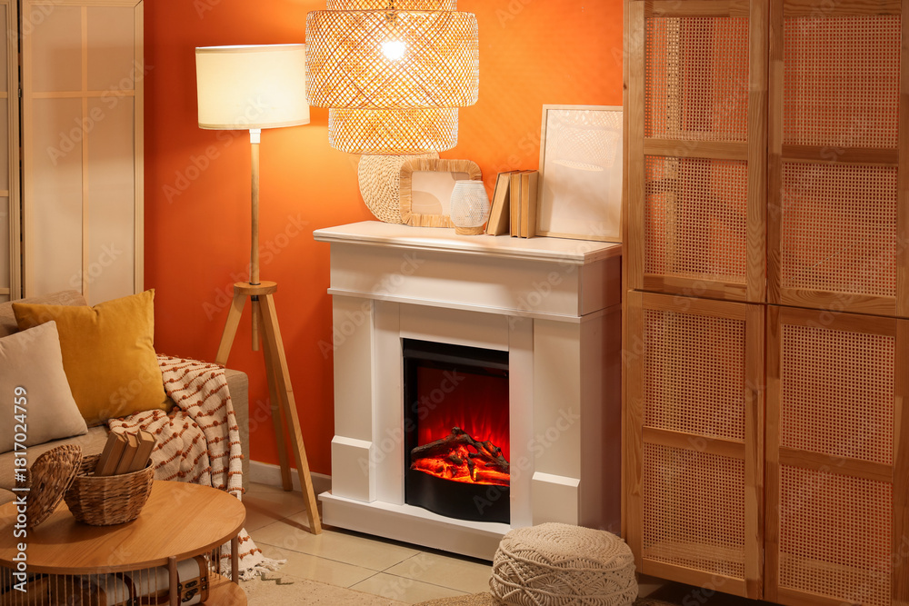Fototapeta premium Fireplace with sofa, closet and glowing lamps near orange wall in living room