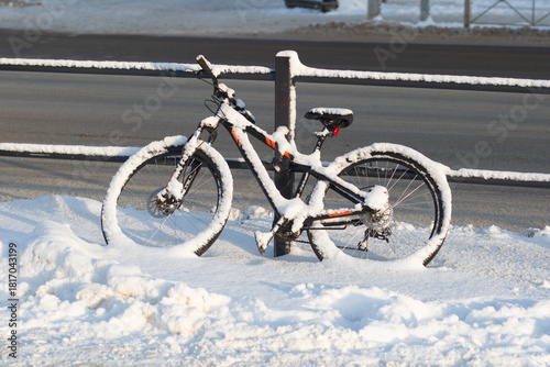 Snowfall. A bicycle in the snow on a city street.