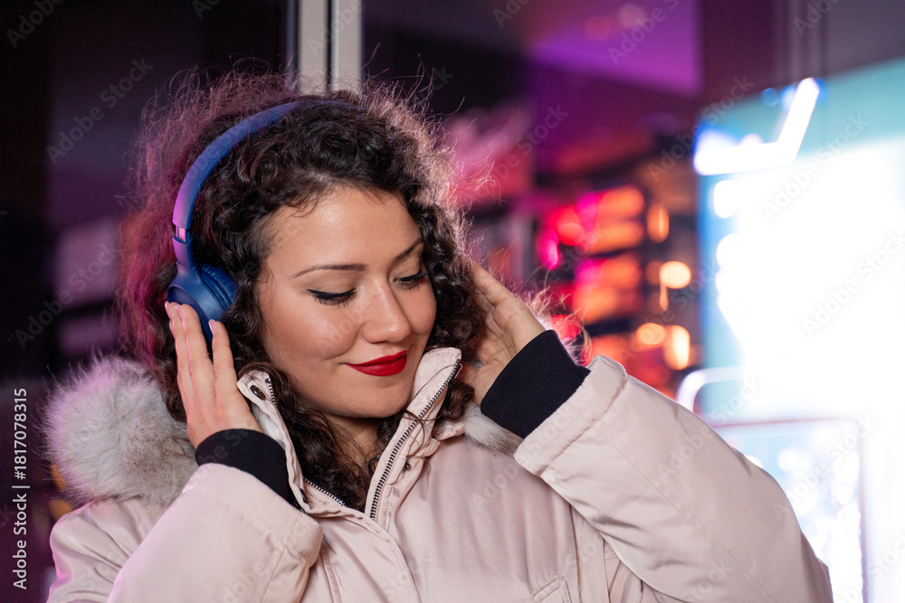 Fototapeta premium Cute charismatic curly hair girl in winter jacket outside, listening to music over headphones