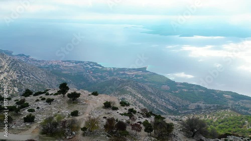 Panoramic view of the stunning Croatian Adriatic coastline from a mountain peak, with islands dotting the cloudy horizon and a charming coastal town below.