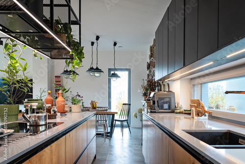 Modern interior kitchen with black luxurious furniture and lamp with shelf over kitchen island. Window near kitchen sink and led lighting. Smart home with design style.