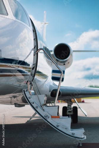 Focus is on the lowered boarding stairs of a small private jet parked on the tarmac of a small airport.