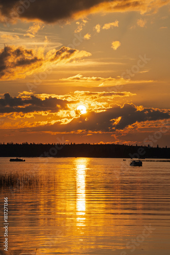 The sun is setting over a lake, with a few boats floating on the water