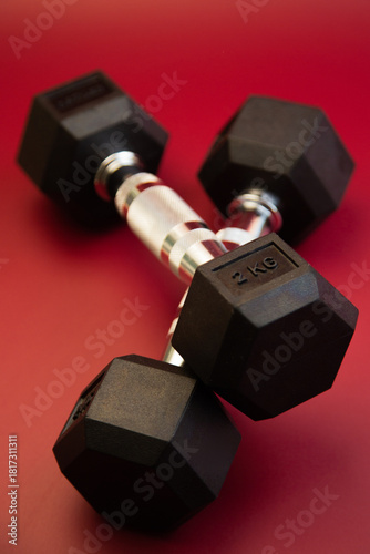 Hexagonal dumbbells with silver accents are positioned on a striking red surface, highlighting fitness gear ideal for strength training and enhancing workout sessions