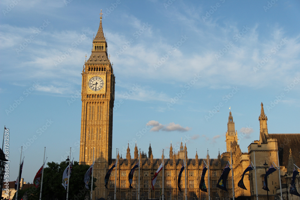 Obraz premium Historic Big Ben clock tower stands tall against a beautiful sunset in London, UK showcasing iconic architecture and vibrant flags
