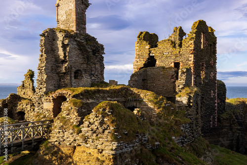 Ruins of Scottish castle Sinclair Girnigoe highlighted by late summer evening sun during golden hour.