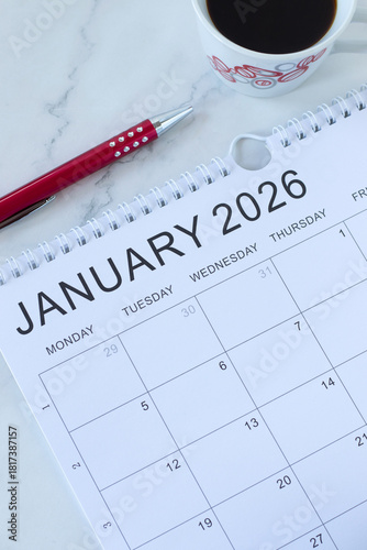 January 2026 new year calendar with pen and coffee cup on a desk. Top view. Annual goals, budget, planning, aspirations, monthly schedule, business concept.