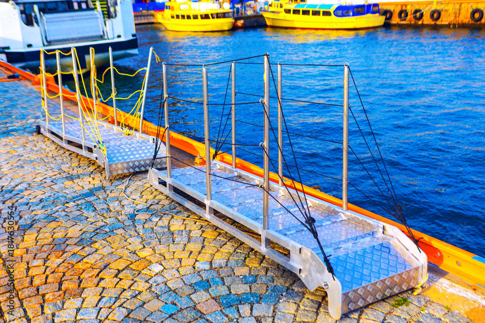 Naklejka premium Aluminum gangways, which are also known as access bridges or passarella, connecting paved dock to the water. Structures provide safe and stable access for people to board or disembark from boats