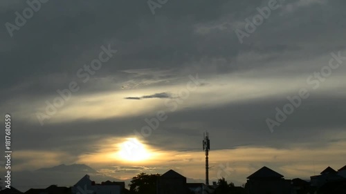 The sun's rays covered by thick clouds rose slowly above the shadow of the mountain and houses, time lapse clouds over the city