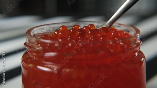 Close-up view of a spoon lifting glossy red caviar from a glass jar, sparkling roe and rich texture, premium seafood delicacy and celebration cuisine concept