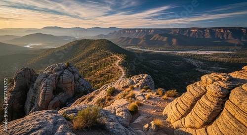 Scenic view of rugged mountains and a curving river surrounded by open grasslands. Peaceful outdoor nature scene captured in soft sunset lighting with rich textures and vibrant colors.