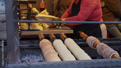 Traditional trdelnik pastry rotates and bakes over open coals at street food market. Process of baking trdelnik in Prague. Concepts of street food and local cuisine