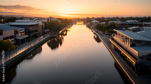 Wide aerial view of a calm river flowing through a city center at sunrise reflecting warm light