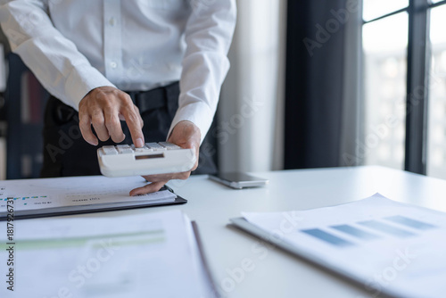 Businessman holding and press botton on calculator over documents