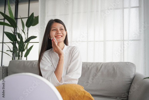 Asian woman in bathrobe applying skincare, take care of your facial skin