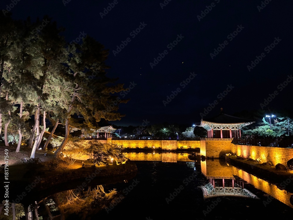 Fototapeta premium Illuminated night view of Donggung Palace and Wolji Pond in Gyeongju, South Korea, showcasing traditional Korean architecture, glowing reflections on calm water, and a serene historic landscape