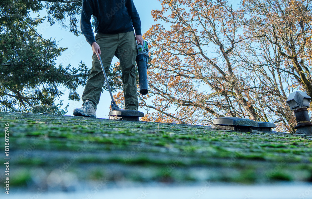 Φωτογραφία Eye-level view of mossy roof with homeowner cleaning it off as part of his yearly home maintenance projects