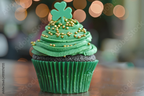 A green-frosted cupcake topped with a shamrock and gold sprinkles, set against warm bokeh lights. Selective focus.