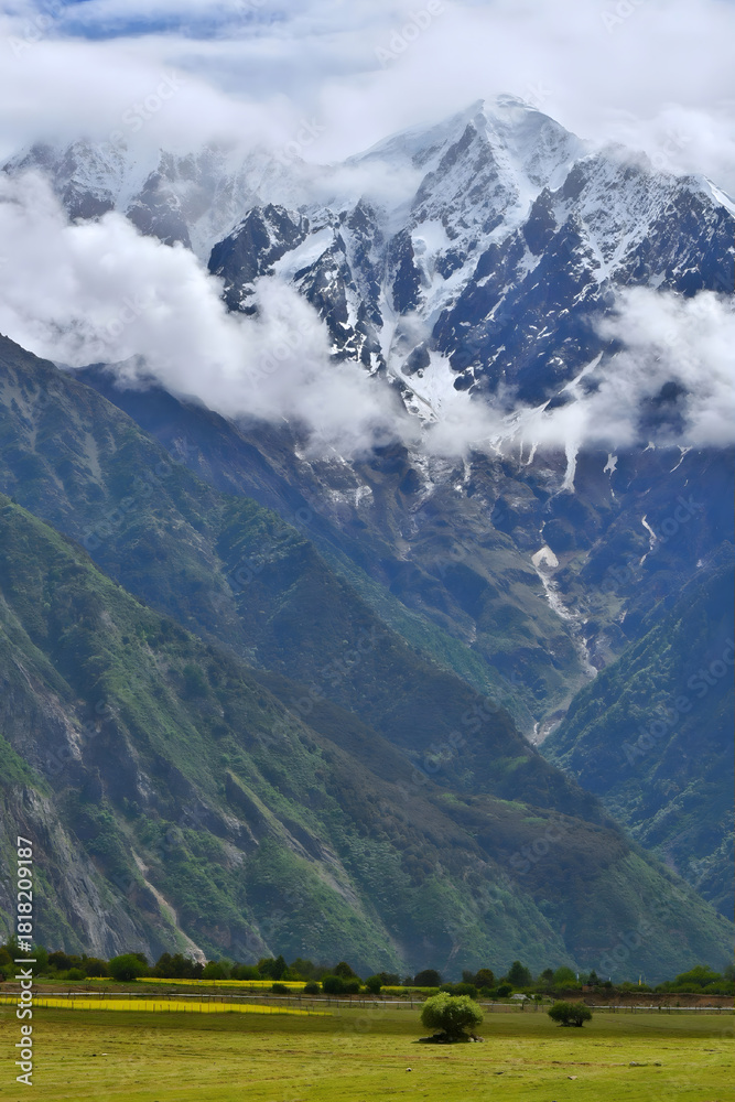 Fototapeta premium Snowcapped Mountain Peaks Above Lush Green Valley with Dramatic Clouds
