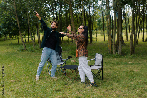 Two friends are having a great time at an outdoor picnic in a lush green area. They are laughing and pointing at something in the distance