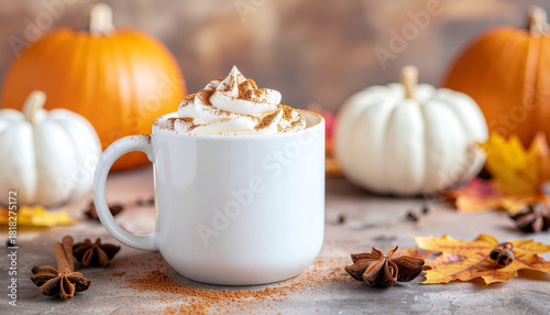 A white mug filled with pumpkin spice latte, topped with whipped cream and cinnamon, surrounded by pumpkins and autumn leaves.