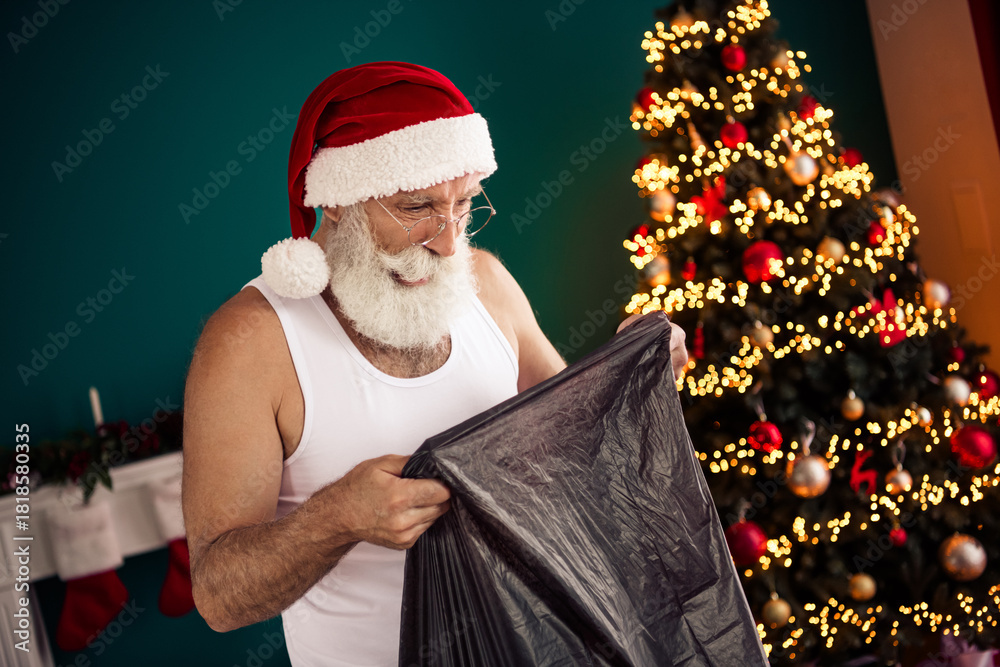 Obraz premium Festive elderly man in a Santa hat tidying up near a decorated Christmas tree at home