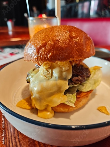 Close-up of a gourmet beef burger with melted cheese and fresh lettuce in a brioche bun, served in a modern restaurant setting. Tasty comfort food and casual dining atmosphere.