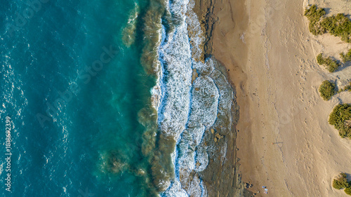 Aerial view of turquoise waves crash against the sandy shore of the Aegean Sea, where golden sands meet the deep blue waters, Rhodes, Greece.