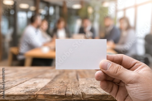 Person hand holding a blank business card template mock up. Ethical business practices. Table with meeting businessman in the office blurred background. Professional networking and communication.