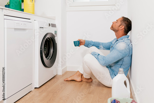 Man relaxing next to washing machine with coffee