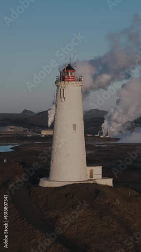 Majestic Reykjanesviti lighthouse, the oldest in Iceland, standing on a rugged volcanic coastline with dramatic steam clouds and soft evening light under a wide Nordic sky.