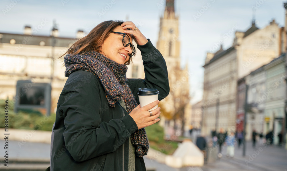 Fototapeta premium Woman in the city. Nice portrait of middle aged woman in eyeglasses holding coffee cup outdoors