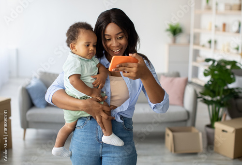 Photos Smiling African American mother holds her little son while enjoying a video call at home