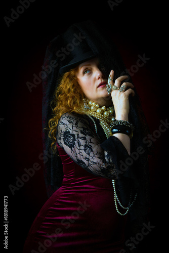 Beautiful woman with long red hair in mourning, with a black top hat and veil, looking out from behind her veil