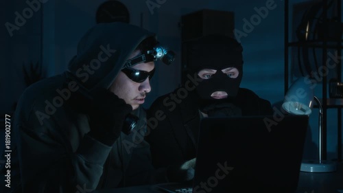 Two young male burglars looking at laptop screen studying confidential information when suddenly turning around upon hearing noise during late-night office break-in