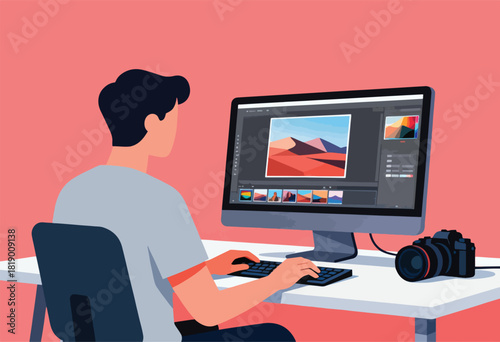 A person works at a desk editing photos on a monitor with a camera nearby, inside a pink room